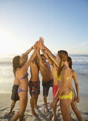 Friends high fiving in circle at beach - CAIF03539