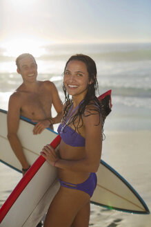 Porträt eines glücklichen Paares mit Surfbrettern am Strand - CAIF03540