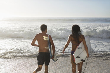 Couple running with surfboards toward ocean - CAIF03541