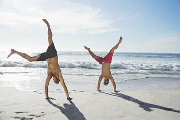 Men in swim trunks doing handstands on beach - CAIF03542