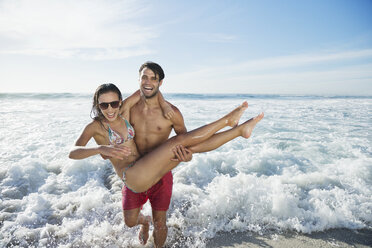 Enthusiastischer Mann trägt Frau am Strand - CAIF03545