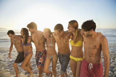 Freunde in Bikinis und Badehosen, die sich umarmen und am Strand spazieren gehen - CAIF03553