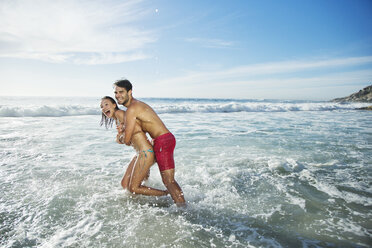 Enthusiastic couple hugging and splashing in ocean - CAIF03555