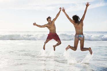 Couple jumping with arms raised on beach - CAIF03559