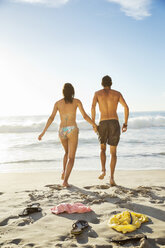 Paar hält sich an den Händen und geht am Strand in Richtung Meer - CAIF03560