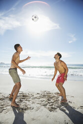 Männer in Badehosen köpfen einen Fußball am Strand - CAIF03561