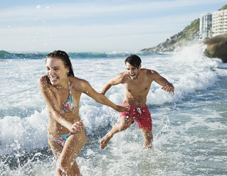 Playful couple splashing in ocean surf - CAIF03567