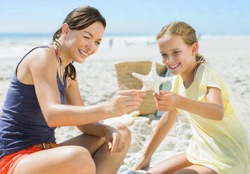 Mutter und Tochter untersuchen Seesterne am Strand - CAIF03579