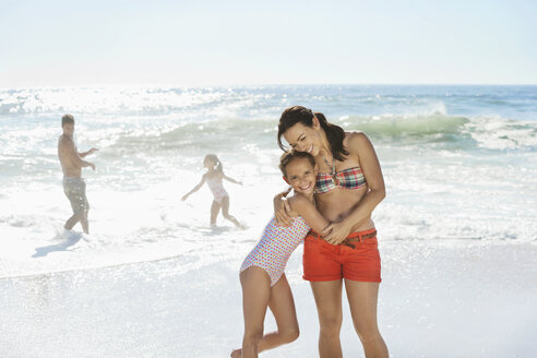 Mother and daughter hugging on beach - CAIF03581