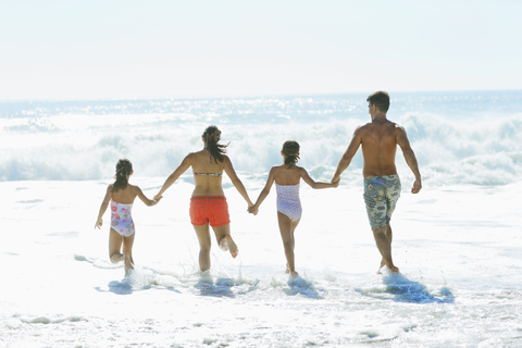 Familie läuft am Strand in die Brandung, lizenzfreies Stockfoto