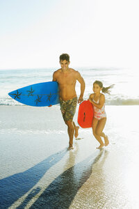 Vater und Tochter tragen Surfbrett und Bodyboard am Strand - CAIF03587