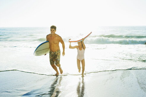 Father and daughter carrying surfboard and bodyboard on beach - CAIF03596