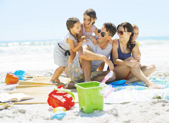 Familie umarmt sich auf einer Decke am Strand - CAIF03601