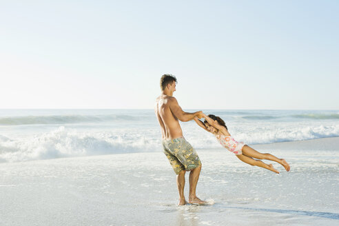 Father swinging daughter in surf at beach - CAIF03604