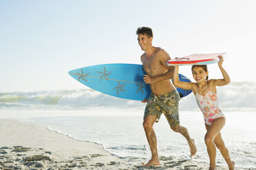 Father and daughter carrying surfboard and bodyboard on beach - CAIF03605