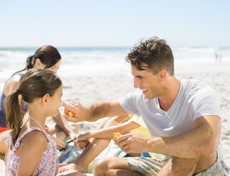 Vater reibt die Nase seiner Tochter am Strand mit Sonnenschutzmittel ein - CAIF03606