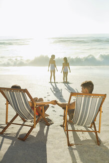 Eltern beobachten Töchter am Strand bei Sonnenuntergang - CAIF03612