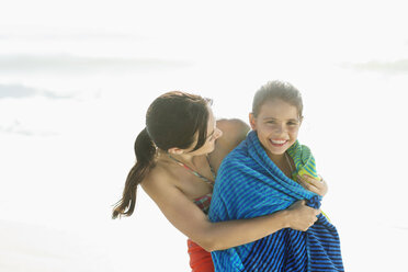 Mother wrapping daughter in towel on beach - CAIF03618