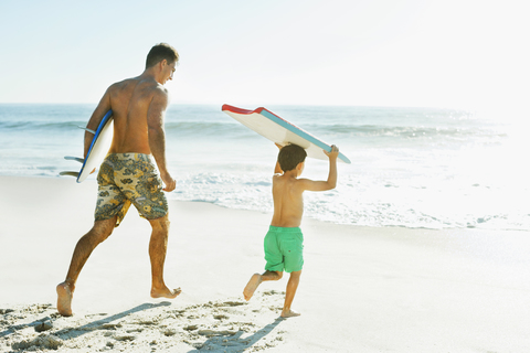 Vater und Sohn tragen Surfbrett und Bodyboard am Strand, lizenzfreies Stockfoto