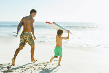 Vater und Sohn tragen Surfbrett und Bodyboard am Strand - CAIF03619