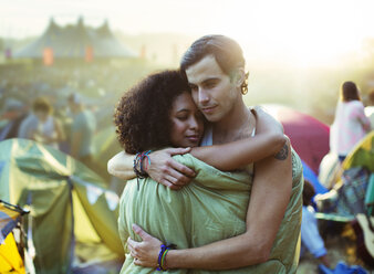 Pärchen im Schlafsack umarmt sich vor Zelten bei Musikfestival - CAIF03632