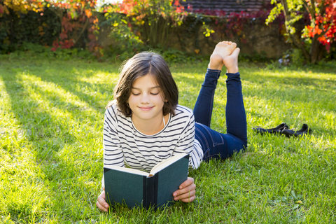 Smiling girl lying on meadow reading a book stock photo