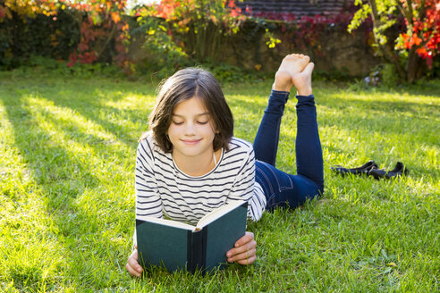 Smiling girl lying on meadow reading a book - LVF06753