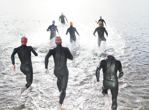 Triathleten in Neoprenanzügen laufen ins Meer, lizenzfreies Stockfoto