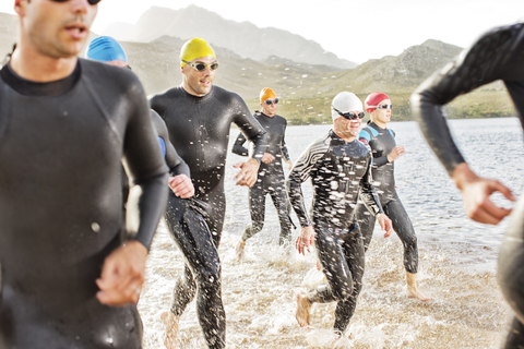 Triathleten in Neoprenanzügen laufen in den Wellen, lizenzfreies Stockfoto