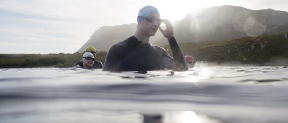 Triathleten in Neoprenanzügen stehen im Wasser - CAIF03828