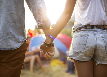 Händchenhaltendes Paar in der Nähe von Zelten auf einem Musikfestival - CAIF03886