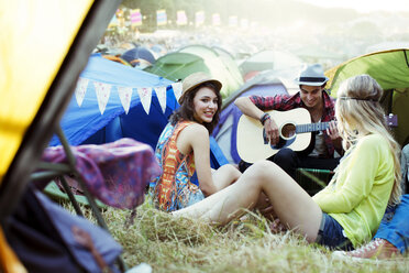 Freunde mit Gitarre hängen in der Nähe von Zelten auf einem Musikfestival herum - CAIF03894