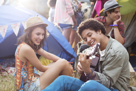 Mann spielt Gitarre vor Zelten auf einem Musikfestival, lizenzfreies Stockfoto