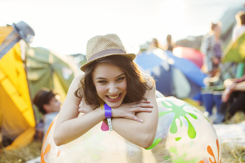 Porträt einer lächelnden Frau, die sich auf einen aufblasbaren Stuhl außerhalb von Zelten bei einem Musikfestival stützt - CAIF03907