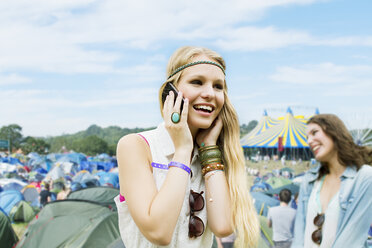 Frau, die außerhalb der Zelte eines Musikfestivals mit einem Handy telefoniert - CAIF03940