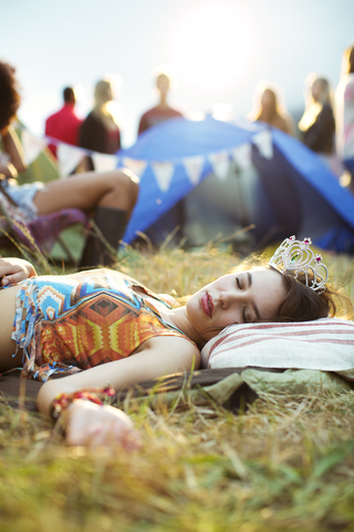 Frau mit Diadem schläft vor dem Zelt bei einem Musikfestival, lizenzfreies Stockfoto