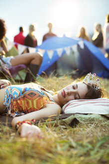 Frau mit Diadem schläft vor dem Zelt bei einem Musikfestival - CAIF03967