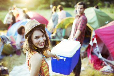 Portrait of woman helping man carry cooler outside tents at music festival - CAIF03978