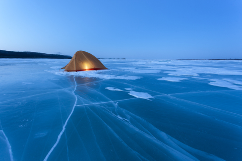 Russland, Oblast Amur, beleuchtetes Zelt auf dem zugefrorenen Fluss Zeya zur blauen Stunde, lizenzfreies Stockfoto