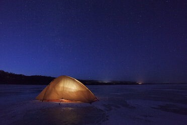 Russia, Amur Oblast, illuminated tent on frozen Zeya River at night under starry sky - VPIF00377