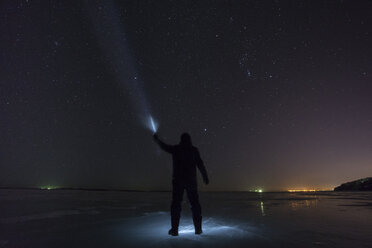 Russland, Oblast Amur, Silhouette eines Mannes mit blauem Strahl, der nachts unter dem Sternenhimmel auf dem zugefrorenen Fluss Zeya steht - VPIF00380