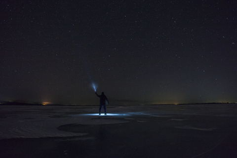 Russia, Amur Oblast, silhouette of man with blue ray standing on frozen Zeya River at night under starry sky stock photo