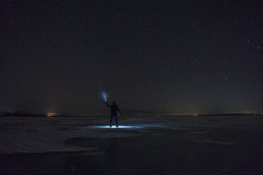 Russland, Oblast Amur, Silhouette eines Mannes mit blauem Strahl, der nachts unter dem Sternenhimmel auf dem zugefrorenen Fluss Zeya steht - VPIF00381