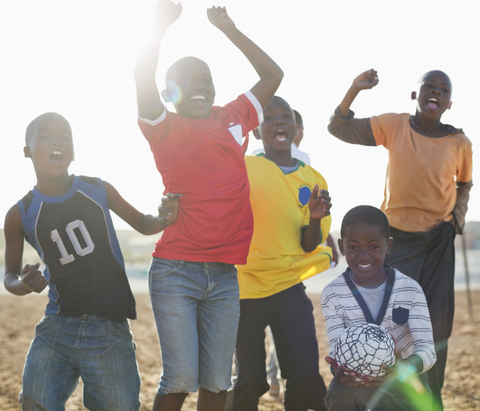 Jungen spielen zusammen Fußball auf einem unbefestigten Feld, lizenzfreies Stockfoto