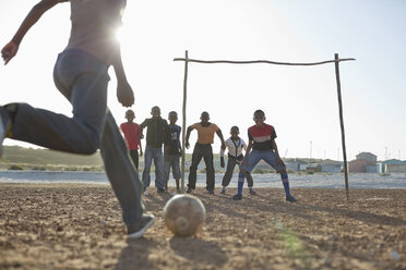 Jungen spielen zusammen Fußball auf einem unbefestigten Feld - CAIF04013