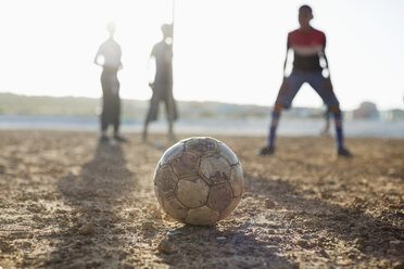 Jungen spielen zusammen Fußball auf einem unbefestigten Feld - CAIF04015