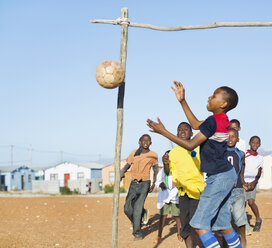 Jungen spielen zusammen Fußball auf einem unbefestigten Feld - CAIF04027