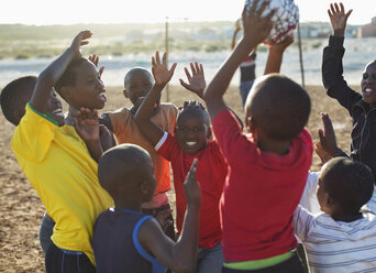 Jungen spielen zusammen Fußball auf einem unbefestigten Feld - CAIF04028
