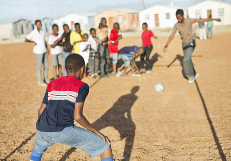 Jungen spielen zusammen Fußball auf einem unbefestigten Feld - CAIF04035