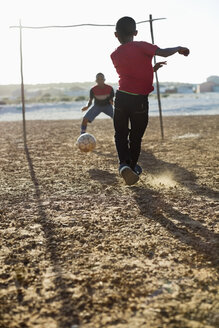 Jungen spielen zusammen Fußball auf einem unbefestigten Feld - CAIF04036